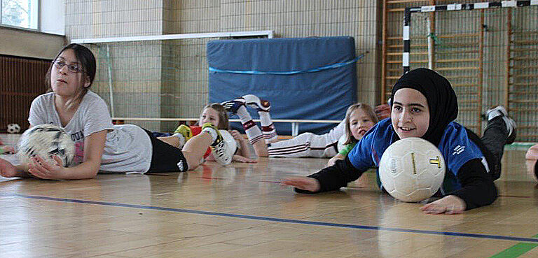 Mädchen liegen auf dem Boden der Sporthalle und machen Ballübungen